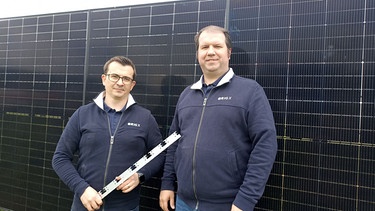 Die Ingenieure Eugen Borgardt (links) und Johann Reis (rechts) mit dem Winkel, mit dem sich Solar-Module an Zäunen aufhängen lassen. | Bild: BR / Eleonore Birkenstock