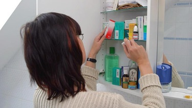 Frau vor Medizinschrank mit diversen Produkten | Bild: mauritius-images